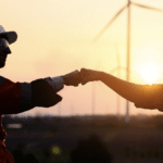 two silhouetted wind turbine technicians give fist bumps in front of wind farm